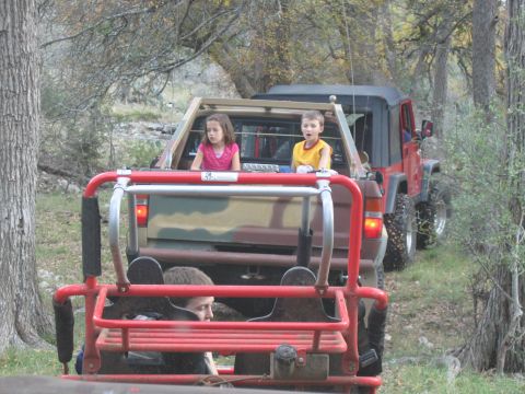 1996 Ford Bronco - Children ride in the back of off-road vehicles as they travel down a wooded trail.