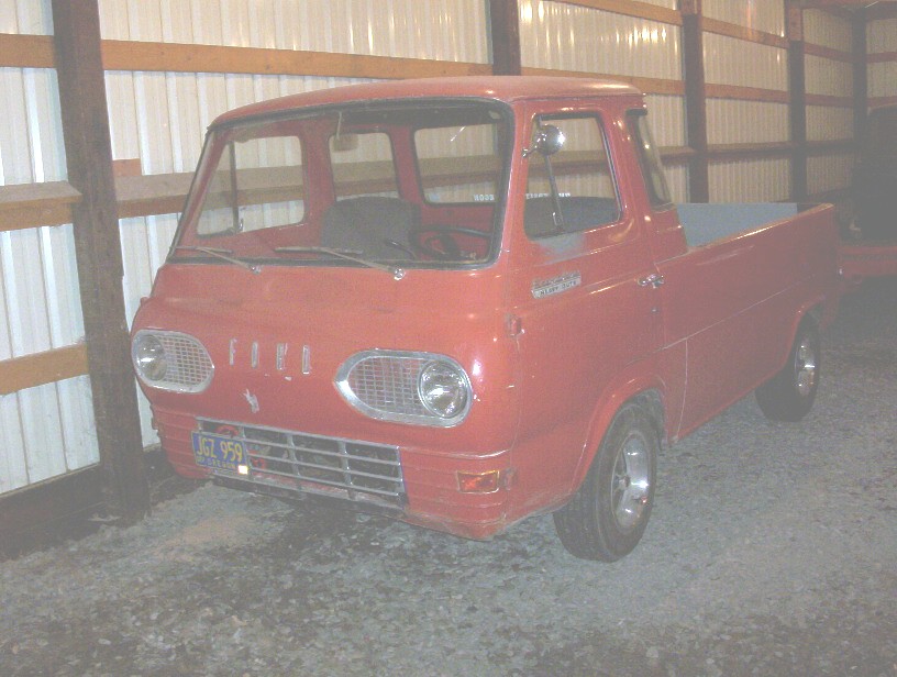 Red Ford Econoline cab-over pickup parked in a metal shed, front 3/4 view