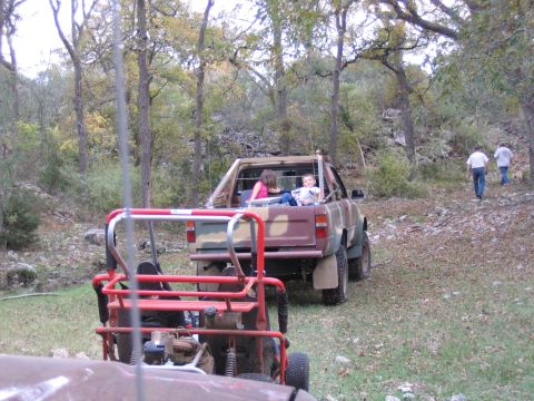 1996 Ford Bronco - A red buggy and a camouflage pickup truck carrying passengers are parked on a wooded trail.