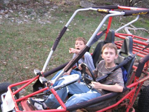 1996 Ford Bronco - Two boys sit in a red go-kart, one pointing ahead while the other looks forward.