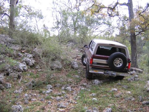 1996 Ford Bronco - A 1996 Ford Bronco navigates a challenging, rocky terrain surrounded by trees.