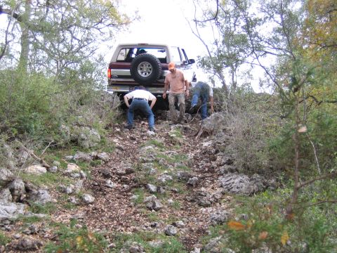 1996 Ford Bronco - Three people are gathered around the rear of a Ford Bronco as it navigates a steep, rocky trail.