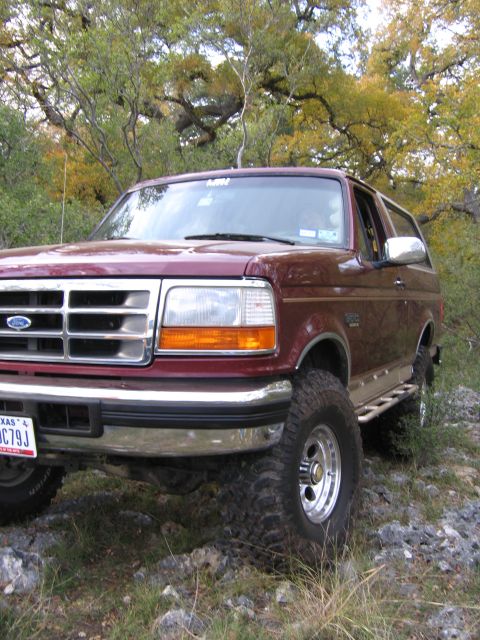 1996 Ford Bronco - This maroon 1996 Ford Bronco, equipped with aftermarket wheels and side steps, is captured in a three-quarter front view while parked on a…