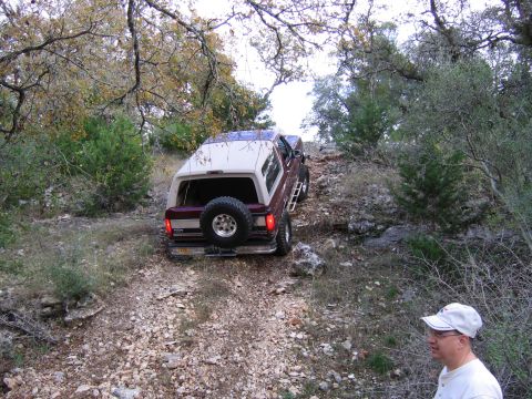 1996 Ford Bronco - A Ford Bronco navigates a challenging off-road path surrounded by trees and rocks.