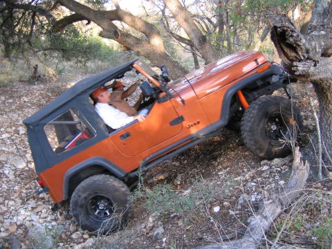 1996 Ford Bronco - Jeep Wrangler navigating a challenging off-road trail with rocky terrain and trees.