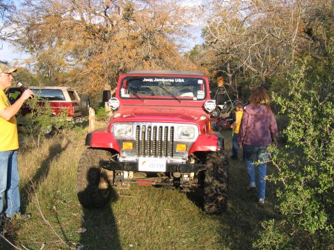 1996 Ford Bronco - A red Jeep Wrangler is seen from the front, parked in a grassy area with trees in the background.