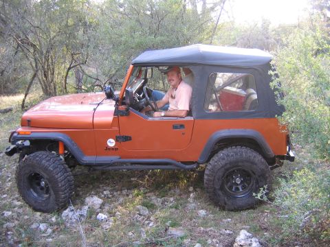 1996 Ford Bronco - Man drives an orange Jeep Wrangler off-road through a wooded area.