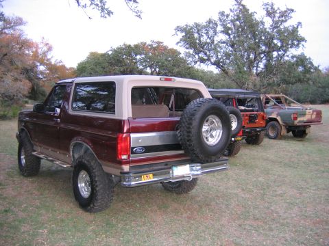 1996 Ford Bronco - Three SUVs are parked in a grassy area with trees in the background.