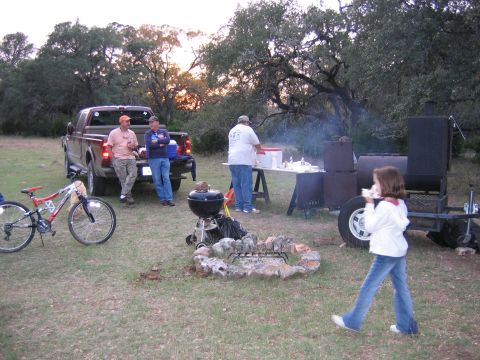1996 Ford Bronco - A group gathers around a picnic table and smoker next to a pickup truck, with a bicycle nearby.