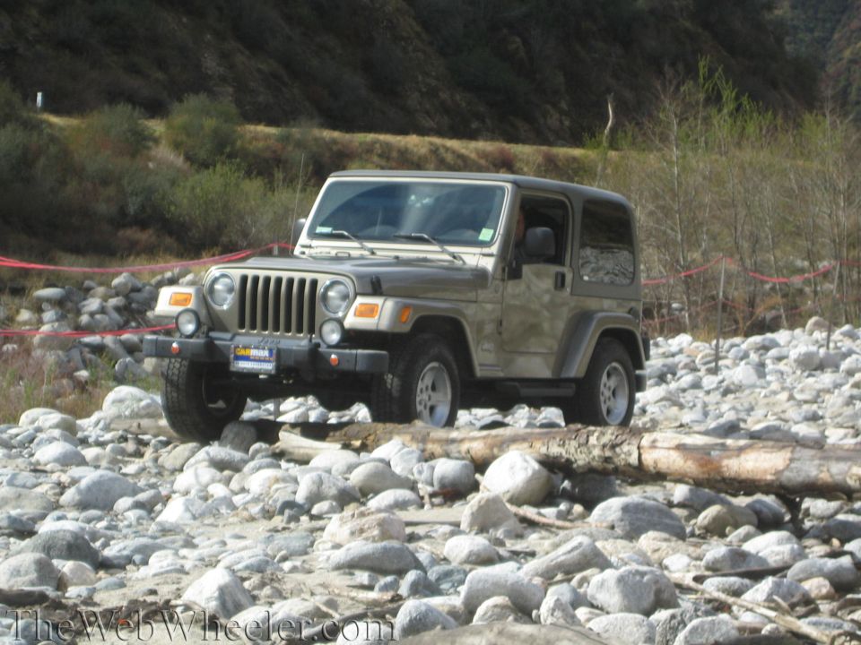 Jeep Wrangler TJ driving over rocks and logs in a dry riverbed
