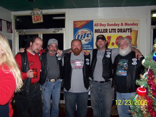 Group of men in leather vests, one holding a beer, with a Christmas tree and bar signs