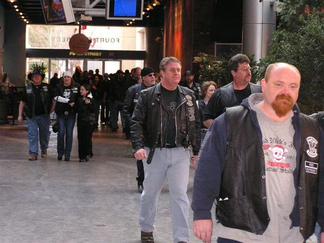 Group of people in leather vests and jackets walking indoors, some with tattoos