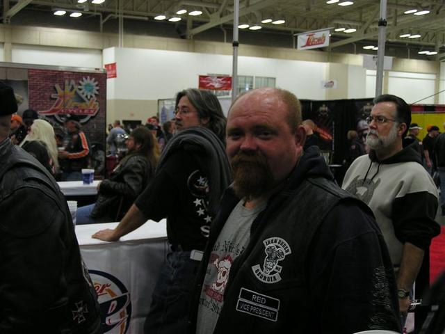 Men at a motorcycle event, one in foreground wears a vest with 'Iron Biker Georgia Red Vice President' patch