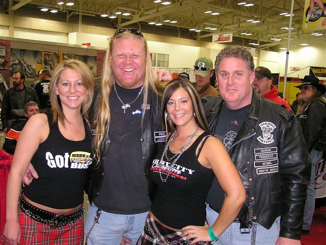 Four people posing for a photo indoors. Two men wear leather vests with patches. Two women wear tank tops