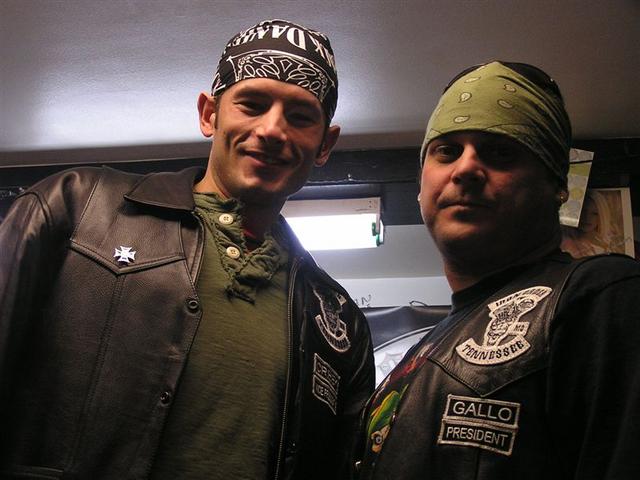 Two men in bandanas and leather jackets, one with a white cross pin, the other with a 'Gallo President' patch