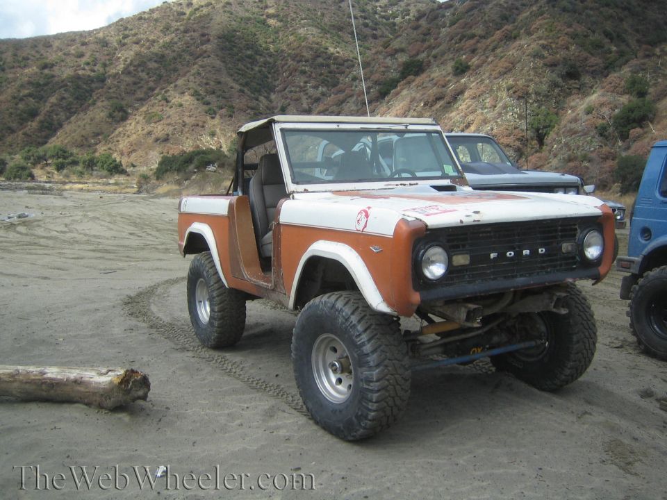 White and orange Ford Bronco with off-road tires, front grille reads "FORD"