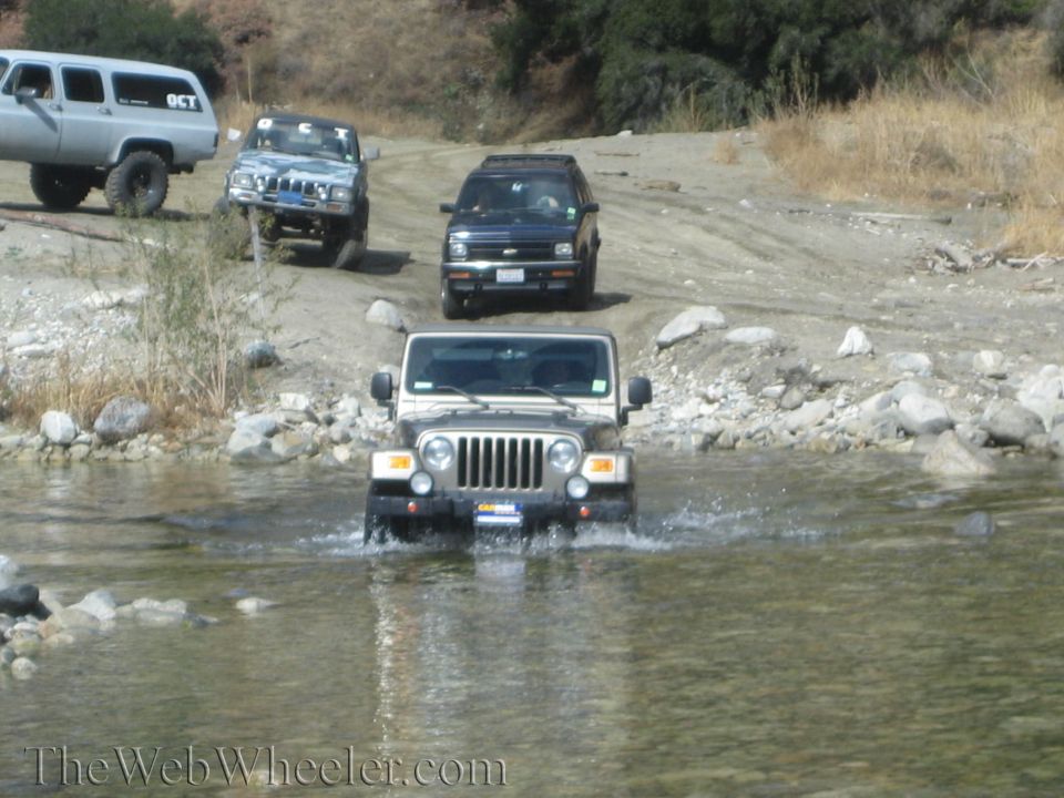 Tan Jeep Wrangler driving through water, other SUVs behind