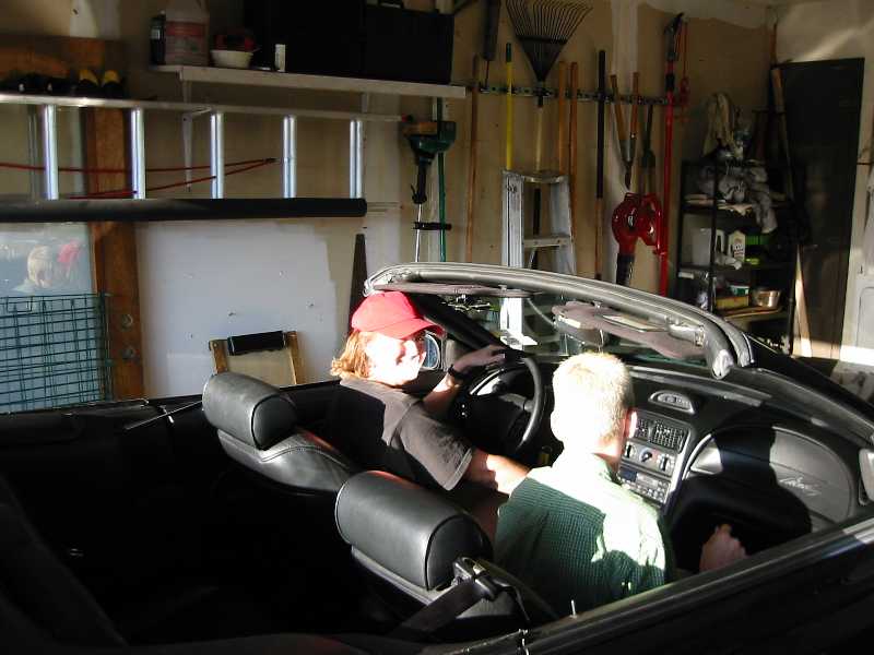 Interior of a black convertible with two people inside, viewed from the rear