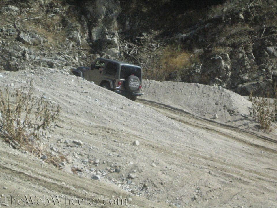 Silver Jeep Wrangler on a dirt hill, spare tire visible on the back