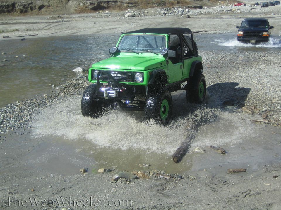 Green Suzuki Samurai driving through water, another SUV in background