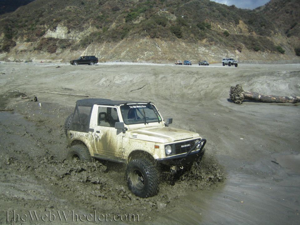 1987 Suzuki Samurai stuck in mud with other vehicles in the background on a dirt road