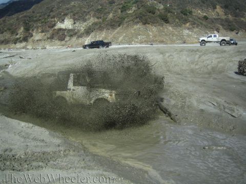 1987 Suzuki Samurai - A 1987 Suzuki Samurai navigates a muddy obstacle, kicking up a large spray.