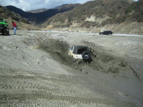 1987 Suzuki Samurai - Off-road vehicles navigate a muddy terrain in a dry riverbed.