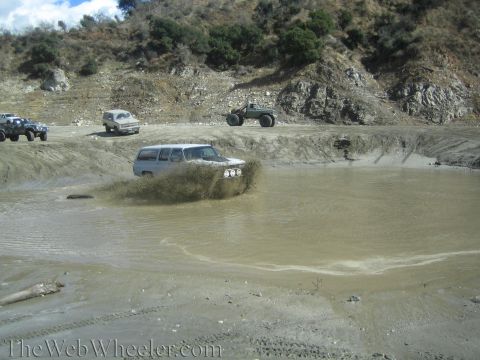 1987 Suzuki Samurai - Multiple off-road vehicles navigate a muddy obstacle course on a sunny day.