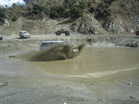 1987 Suzuki Samurai - Several off-road vehicles navigate a muddy pit, creating large splashes.