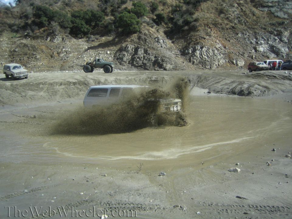 White SUV splashing mud in a muddy pool, front grille and headlights visible