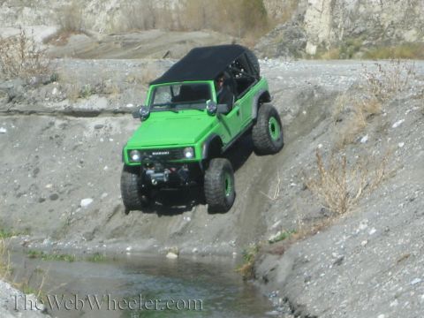 1987 Suzuki Samurai - This green Suzuki Samurai is navigating a challenging off-road course, descending into a water obstacle.