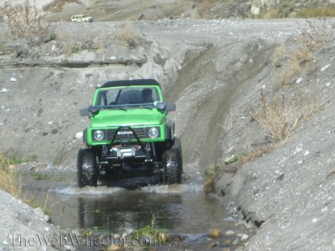 1987 Suzuki Samurai - A green 1987 Suzuki Samurai navigates a water-filled path in a , off-road environment.