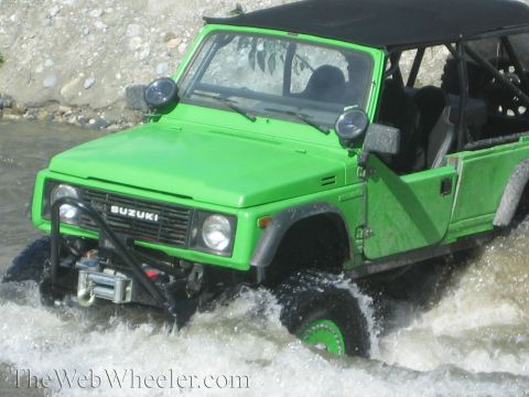 1987 Suzuki Samurai - A bright green Suzuki Samurai navigates through a shallow body of water, kicking up spray.