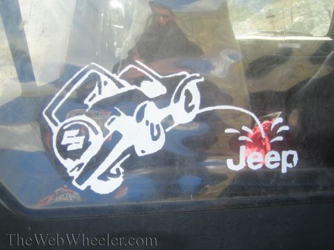 1987 Suzuki Samurai - A humorous sticker on a vehicle window depicts a cartoon character urinating on a Suzuki logo, with the word "Jeep" visible.