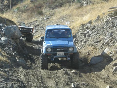 1987 Suzuki Samurai - A blue 1987 Suzuki Samurai navigates a rocky off-road trail, with another vehicle visible behind it.