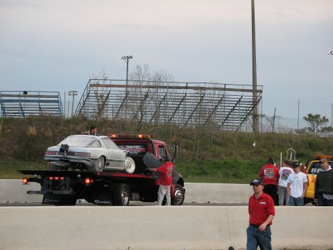 2006 Mazda 6 - A white coupe is loaded onto a flatbed truck, with a group of people standing nearby.