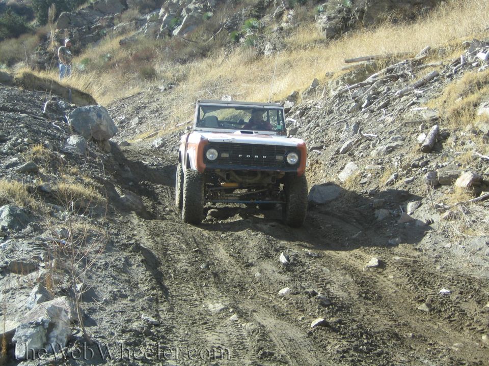 White and orange Ford Bronco climbing a steep dirt trail with large tires