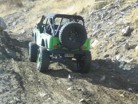 1987 Suzuki Samurai - A green off-road vehicle navigates a dusty, rocky trail with a spare tire mounted on the rear.