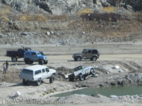 1987 Suzuki Samurai - Multiple off-road vehicles navigate a challenging terrain with water and dirt obstacles.