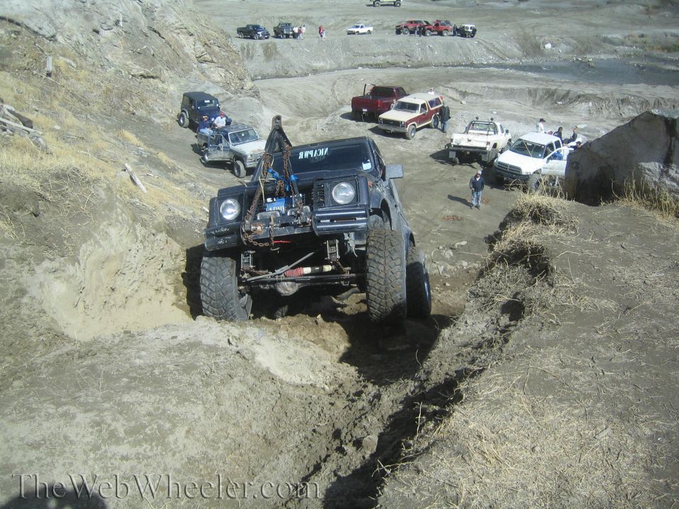 Black 1987 Suzuki Samurai off-roading in mud, front view, hood open, modified engine