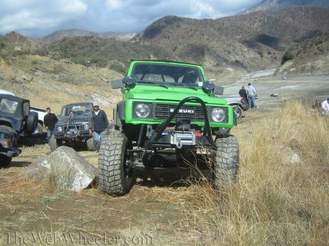 1987 Suzuki Samurai - A lifted green 1987 Suzuki Samurai is parked outdoors with other vehicles in a dry, mountainous area.