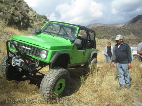 1987 Suzuki Samurai - Modified 1987 Suzuki Samurai tackling an off-road trail with people nearby.