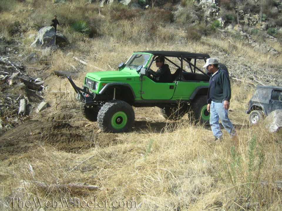 Green 1987 Suzuki Samurai with off-road tires and roll cage on a dirt trail