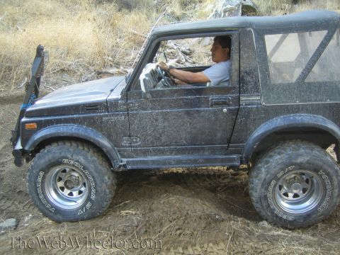 1987 Suzuki Samurai - A driver navigates a black 1987 Suzuki Samurai through a muddy, off-road terrain.