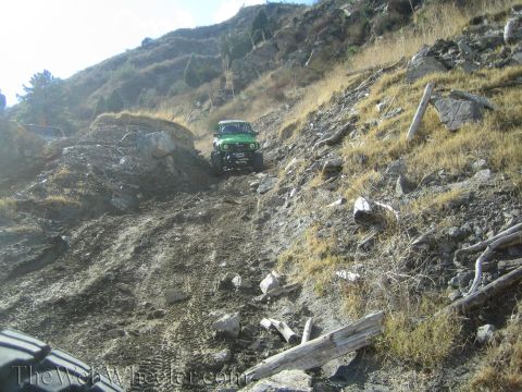 1987 Suzuki Samurai - A green off-road vehicle navigates a steep, rocky incline on a sunny day.