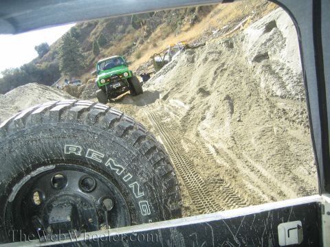 1987 Suzuki Samurai - A green off-road vehicle navigates a steep, sandy incline, with another vehicle partially visible in the background.