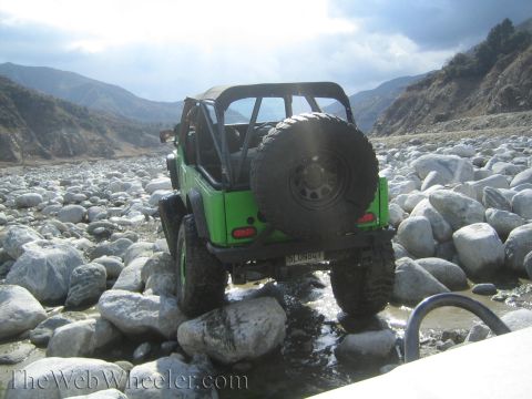 1987 Suzuki Samurai - Off-roading in a 1987 Suzuki Samurai through a rocky riverbed with a mountainous backdrop.