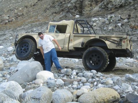 1987 Suzuki Samurai - A man stands beside a tan off-road truck navigating rocky terrain.