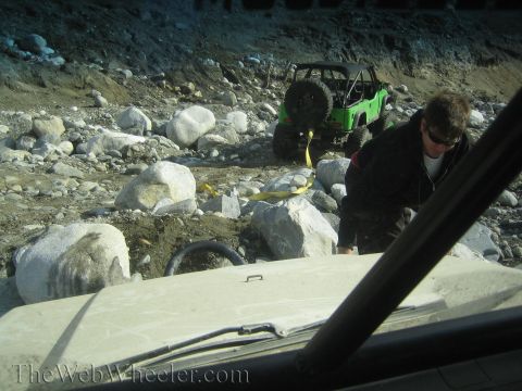 1987 Suzuki Samurai - Two off-road vehicles are stuck in a rocky area, with a person attempting to use a tow strap.
