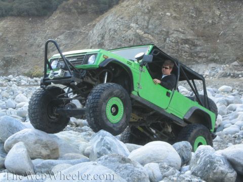 1987 Suzuki Samurai - A green 1987 Suzuki Samurai navigates a rocky terrain with its front-left tire elevated.